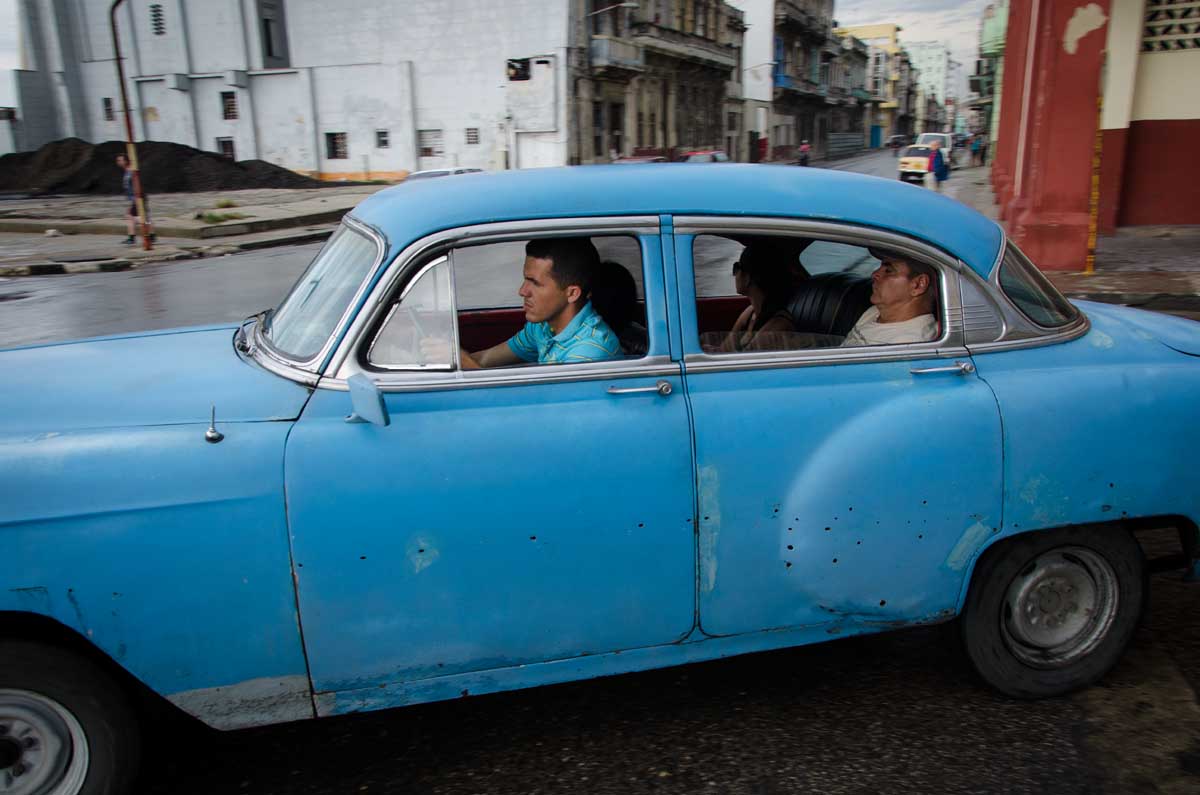 street photography in havana about an old american car with people sleeping inside